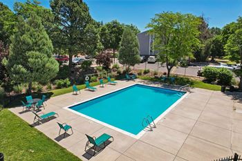 A swimming pool surrounded by green trees and lawn chairs